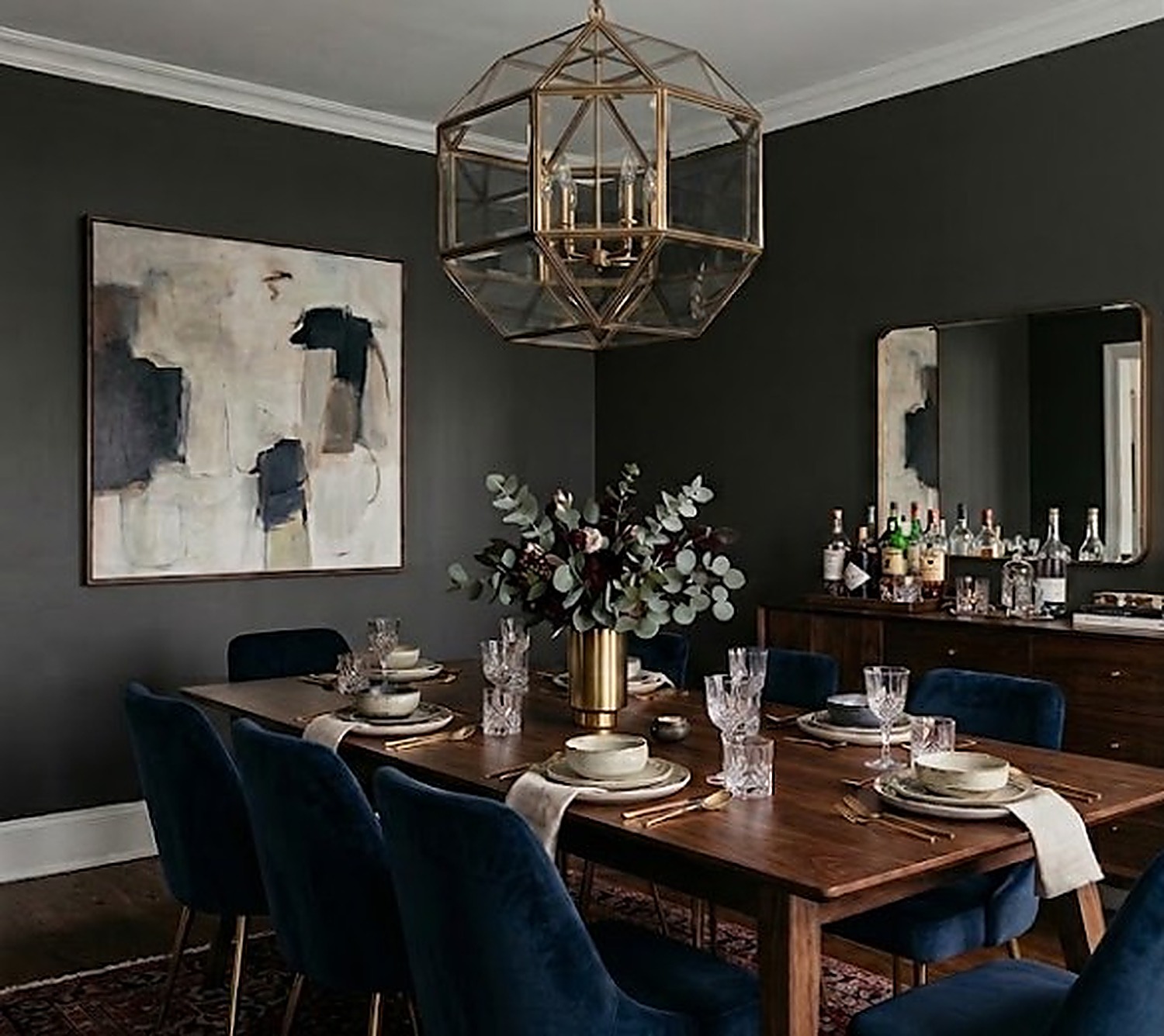 Detail of a brass geometric pendant light fixture over a moody emerald dining room